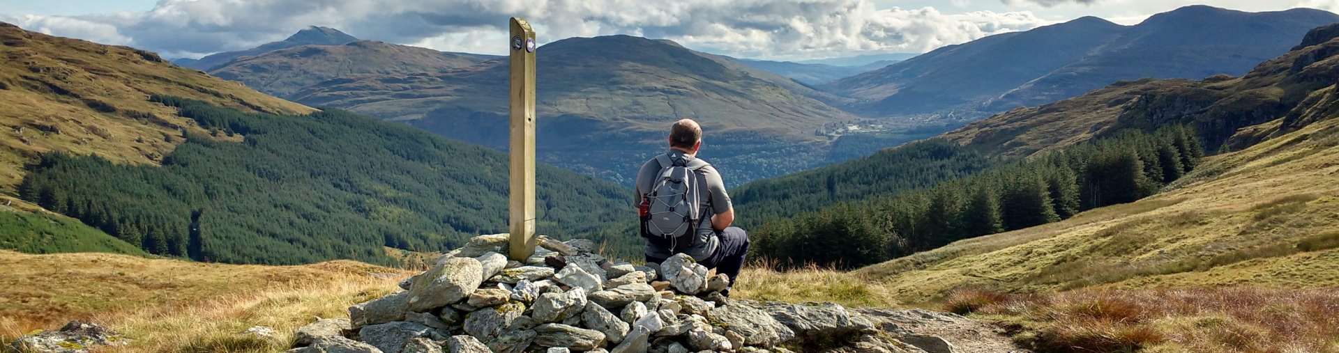 A walker sits at a waymarker overlooking a forested valley - tranquil holidays with corporate discounts